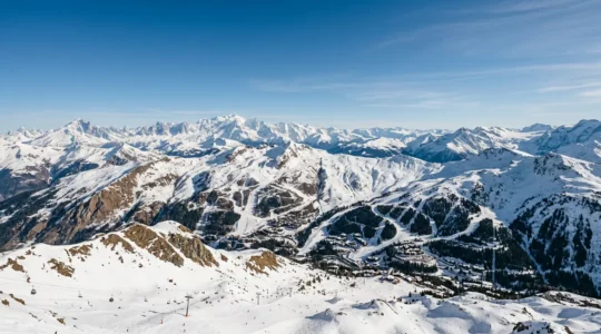 Panorama majestueux des sommets alpins enneigés sous un ciel bleu avec domaines skiables visibles