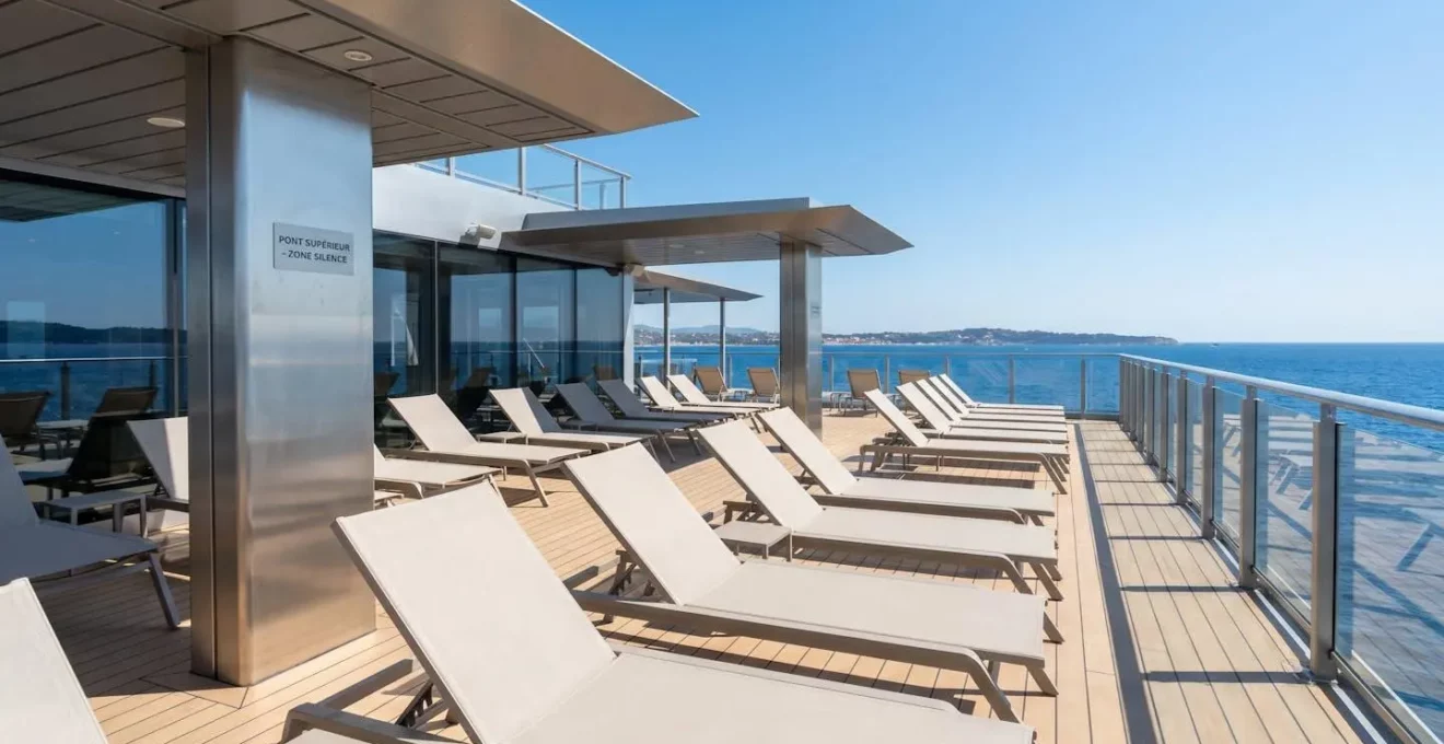 Pont extérieur d'un ferry moderne avec vue dégagée sur la mer Méditerranée, chaises longues vides alignées sous un ciel bleu éclatant